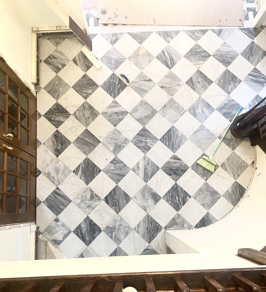 Installation in progress of classic checkerboard foyer flooring, with stone tiles being carefully laid during the Tudor home renovation in Sparta, NJ. 