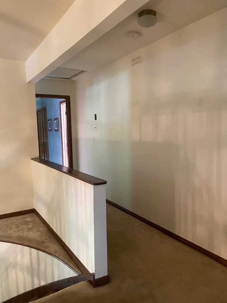 Staircase landing before renovation, featuring a sheetrock half-wall railing that enclosed the space and limited openness.