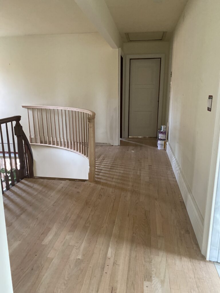 Staircase landing during renovation, showing the updated railing with newly installed curved spindles replacing the former sheetrock half-wall.